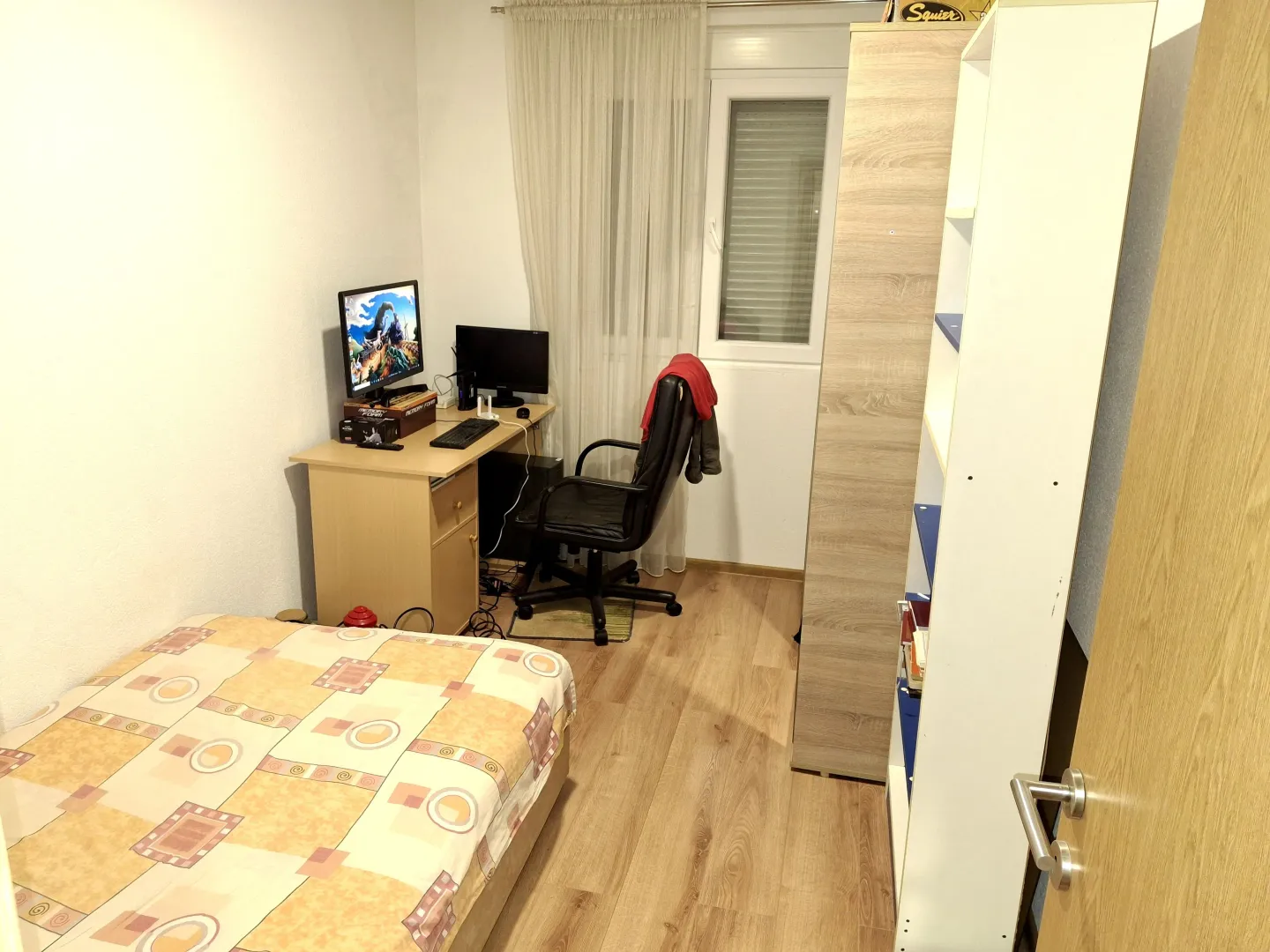 Manja spavaća soba sa krevetom, radnim stolom i garderoberom.