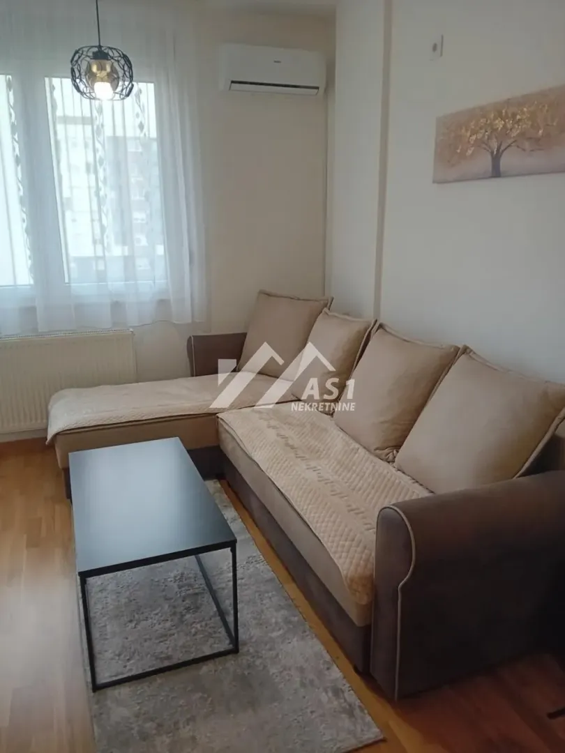 Dnevna soba sa ugaonom garniturom, klub stočićem i prozorom.
