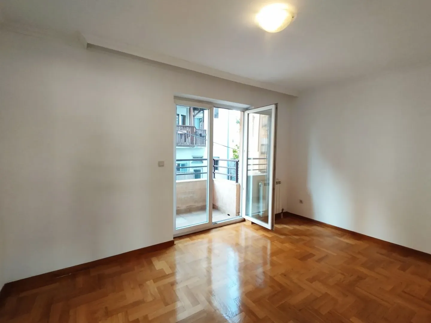 Prazna soba sa parketom i izlazom na balkon.