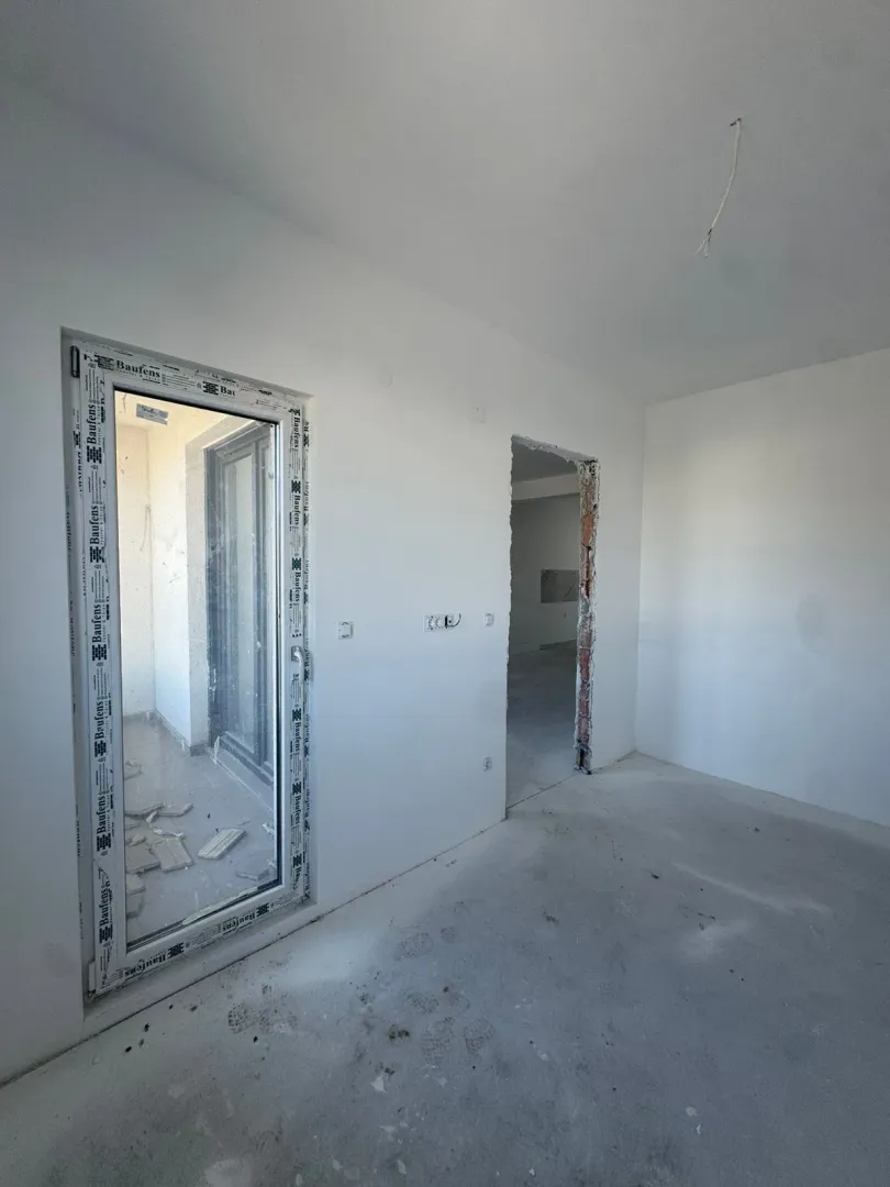 Unutrašnjost prostorije u izgradnji sa belim zidovima i balkonskim vratima.
