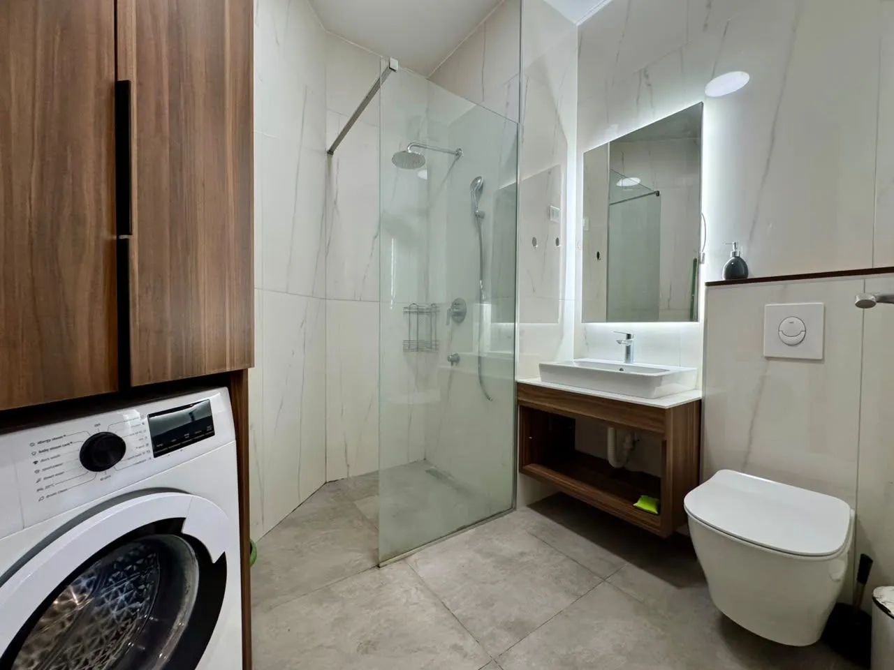 Modern bathroom equipped with a walk-in shower, washbasin, toilet, and washing machine.