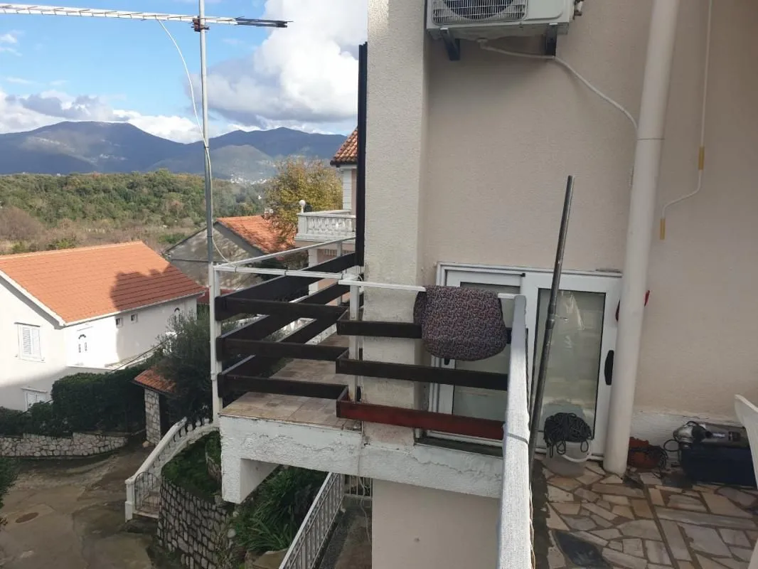 Balkon sa pogledom na okolne kuće i planine u pozadini.