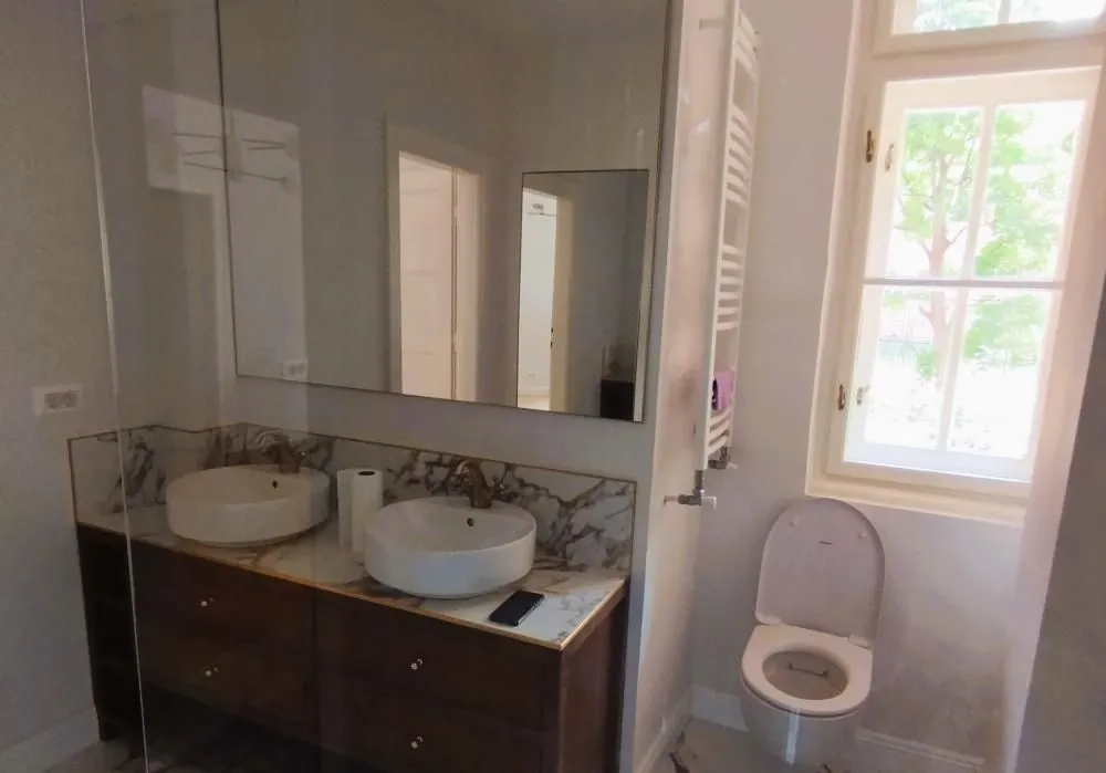 Modern bathroom with double sinks, large mirror, and toilet.