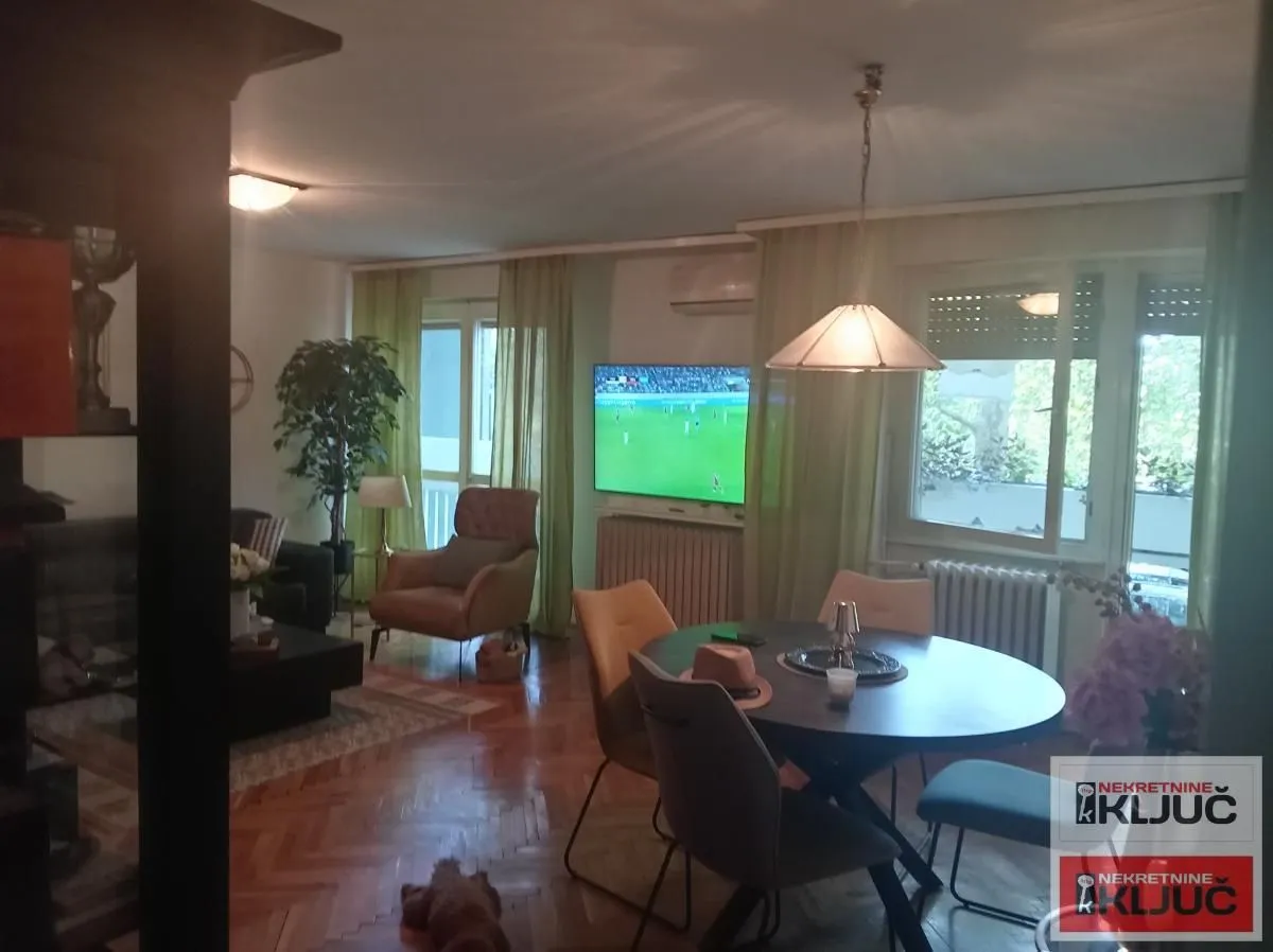 Dnevna soba sa trpezarijom, garniturom i televizorom na zidu.