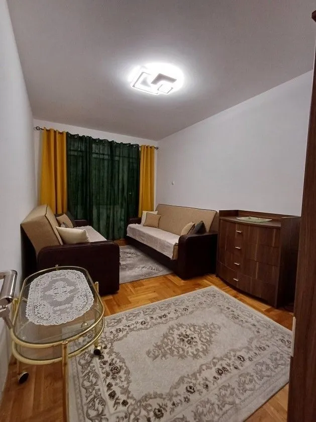 Svijetla dnevna soba sa dva kauča, komodom i tepihom.