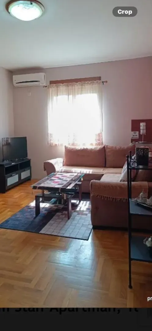 Dnevna soba sa garniturom, stočićem, televizorom i parketom na podu.
