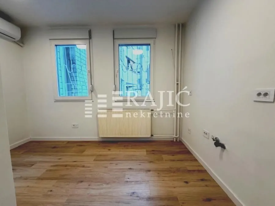 Empty room with wooden flooring and two windows.