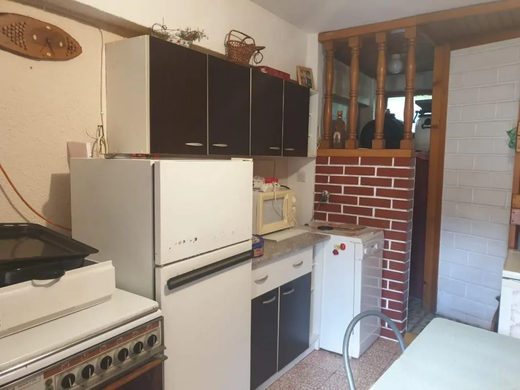 Manja kuhinja sa drvenim elementima, frižiderom i šporetom.