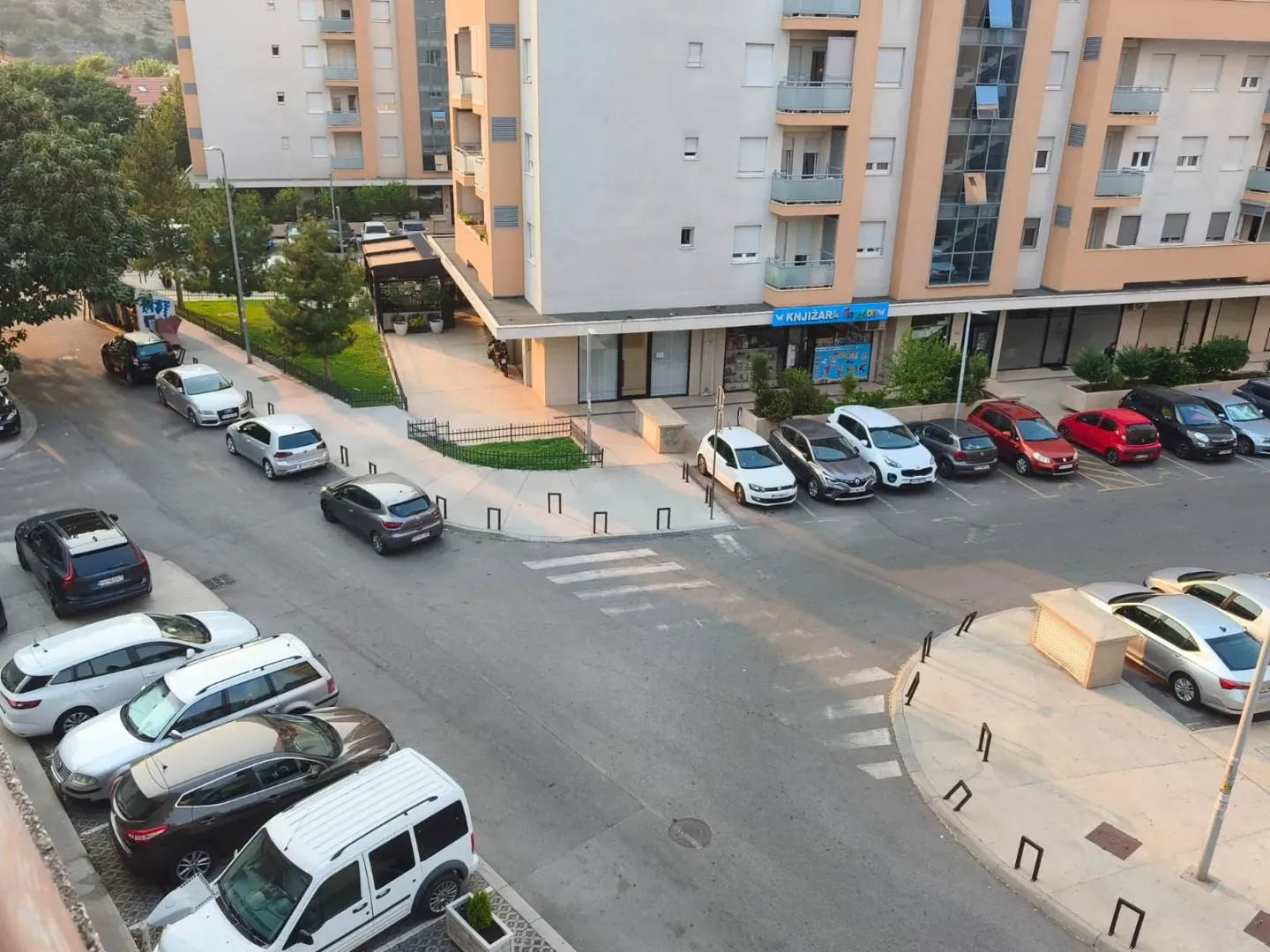 Pogled iz stana na ulicu sa parkiranim automobilima i okolnim zgradama.