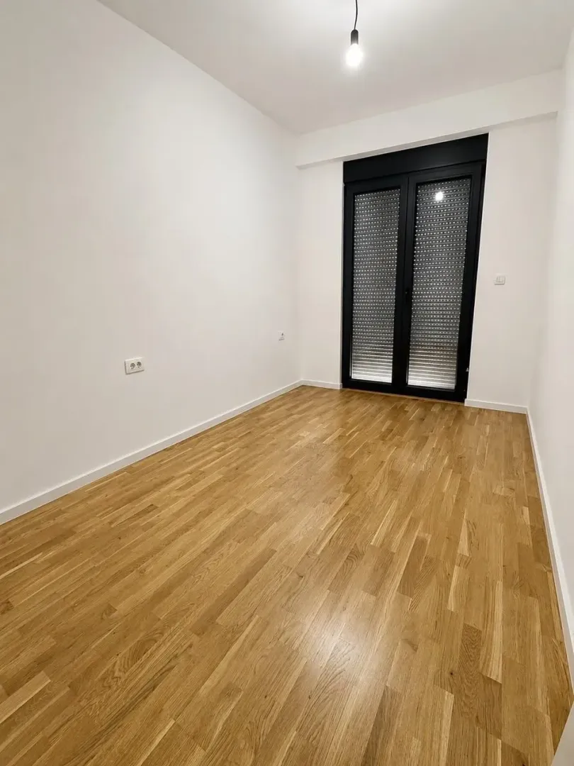 Prazna soba sa parketom i balkonskim vratima.