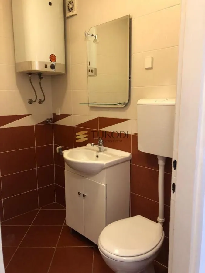 Manje kupatilo sa lavaboom, wc šoljom i bojlerom na zidu.