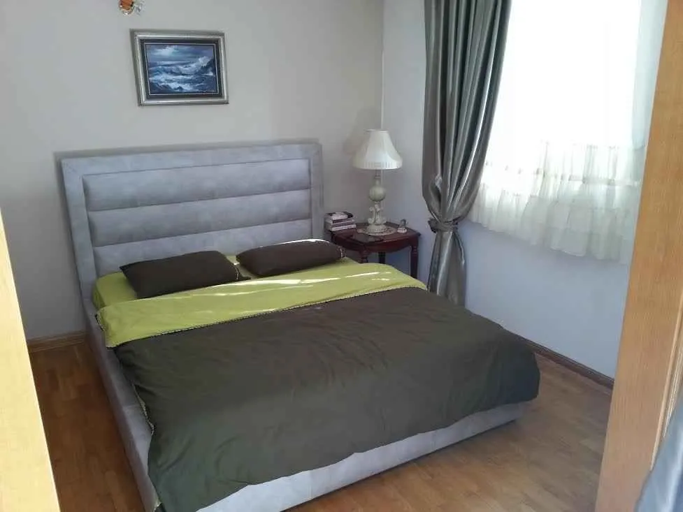 Namještena spavaća soba sa bračnim krevetom, noćnim stočićem i prozorom.