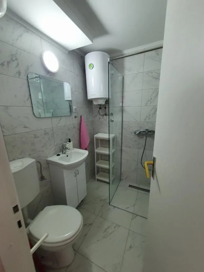 Manje kupatilo sa tuš kabinom, umivaonikom i wc šoljom obloženo mermernim pločicama.