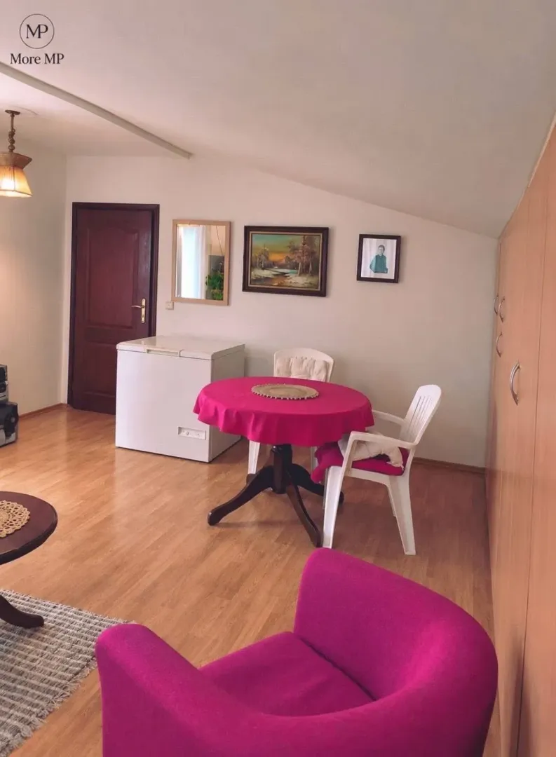 Dnevni boravak sa trpezarijskim stolom i roze foteljom.