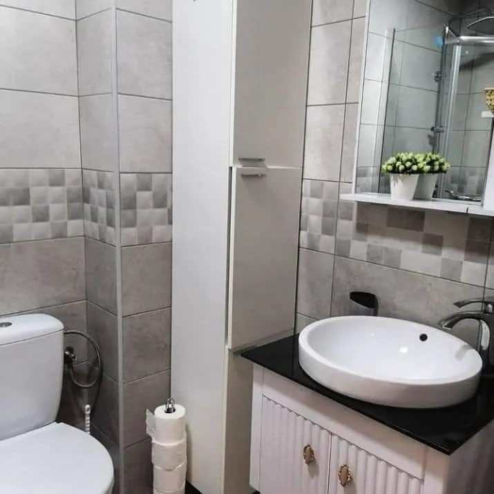 Modern bathroom with a white sink, cabinet, and grey tiles.