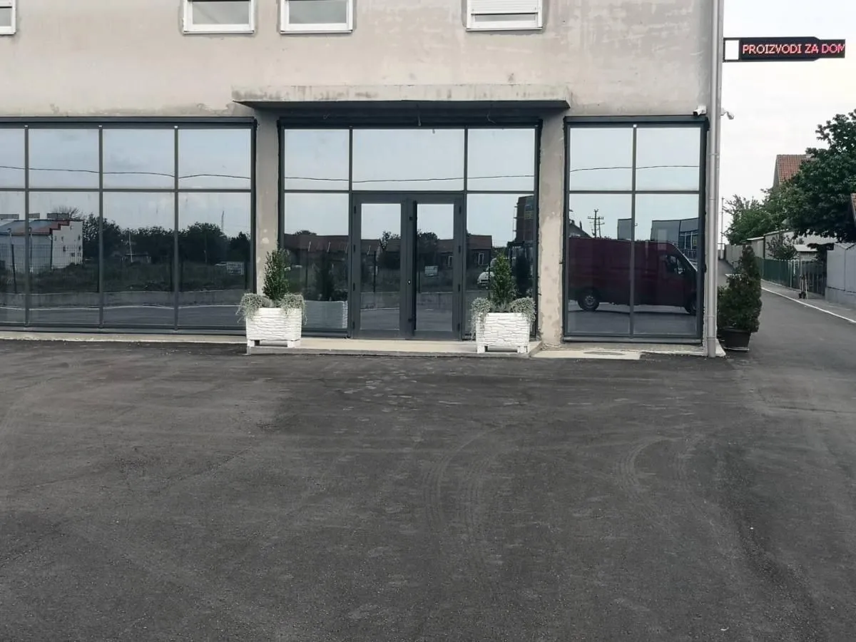 View of the exterior of a commercial building with large glass display windows and an asphalt parking lot.