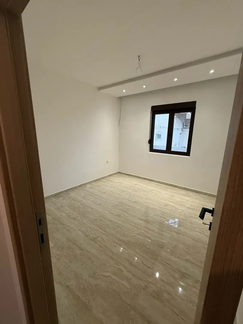 Pogled kroz vrata na praznu prostoriju sa pločicama na podu i spuštenim plafonom.