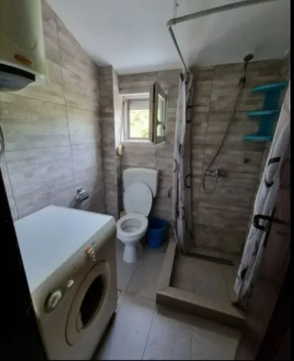 Jednostavno kupatilo sa tuš kabinom, toaletom i veš mašinom.