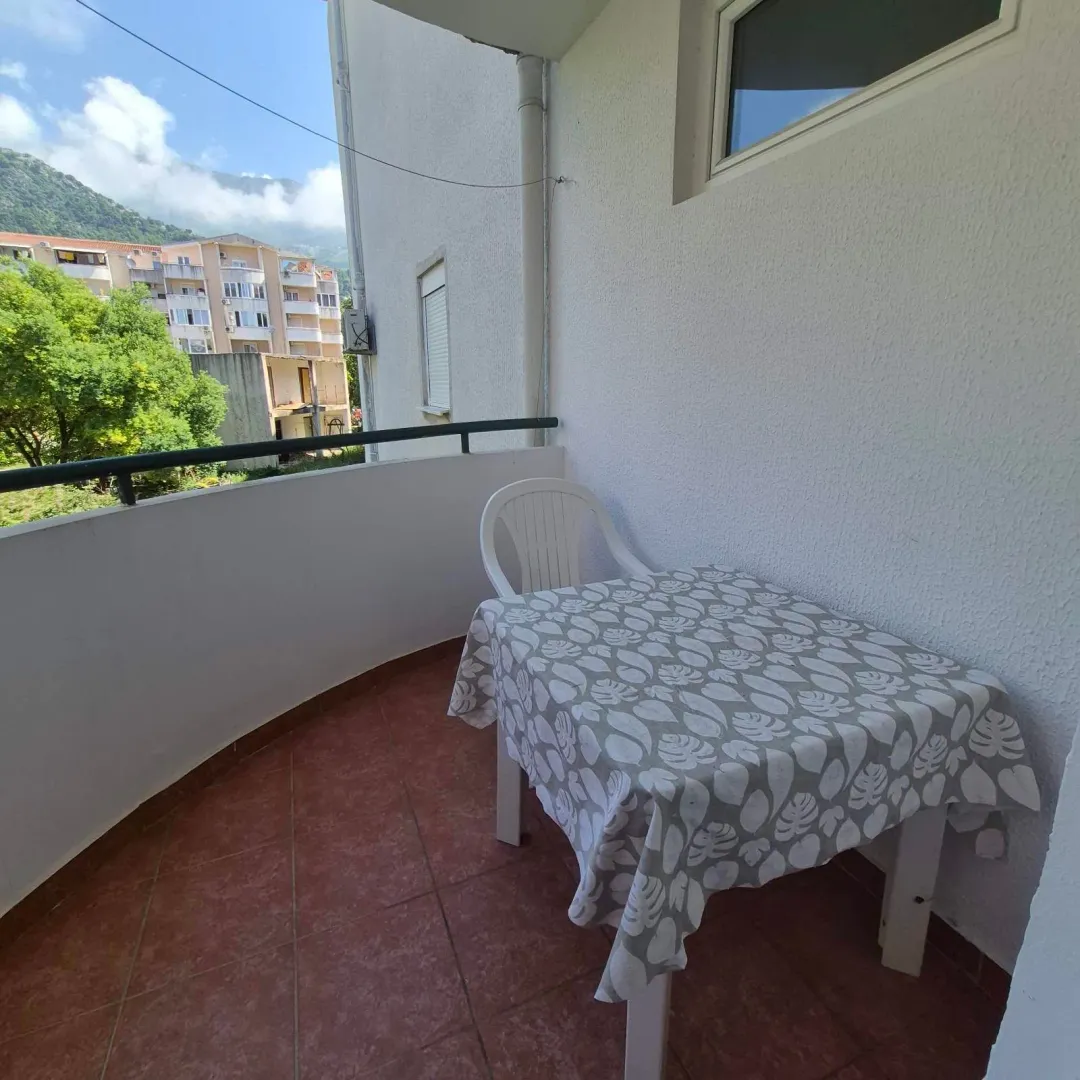 Small balcony with a table, chairs, and a view of surrounding buildings and hills.