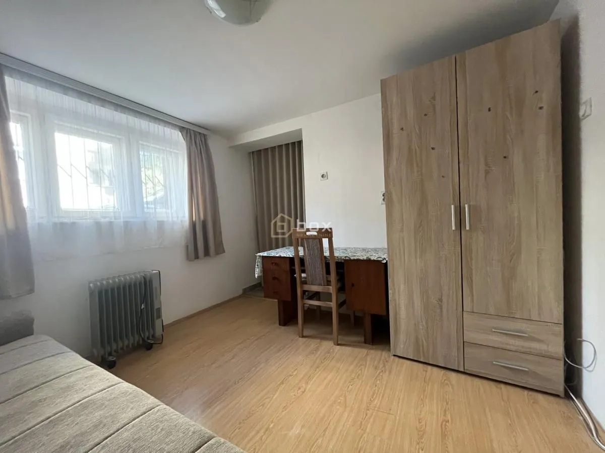 Nameštena spavaća soba sa krevetom, velikim drvenim ormarom, pisaći sto i prozorom.