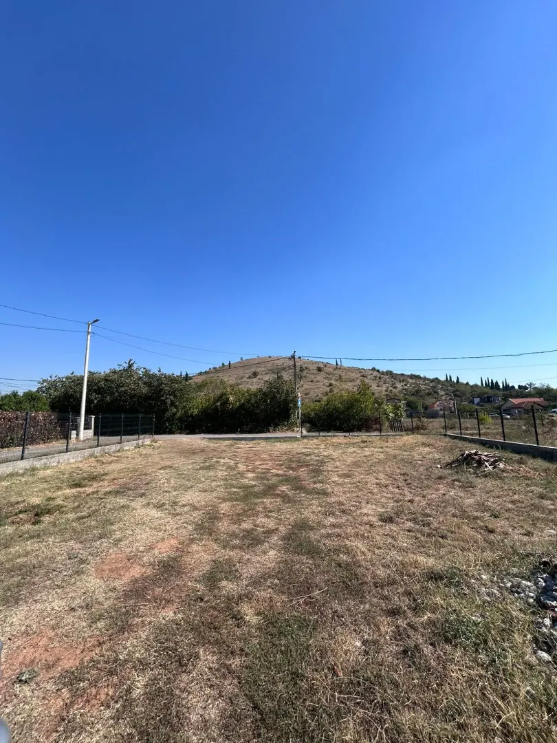 Pogled na ograđeni plac sa travnatom površinom i brdom u pozadini.