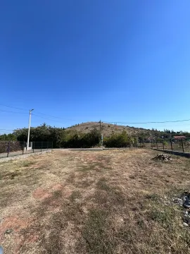 Pogled na ograđeni plac sa travnatom površinom i brdom u pozadini. - image 6