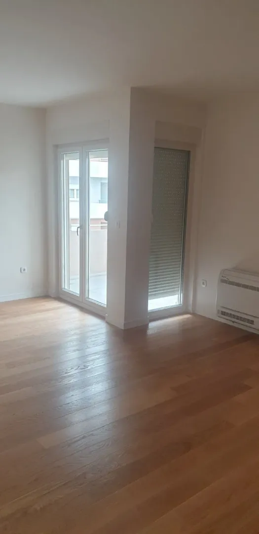 Empty room with light parquet flooring and access to a balcony.