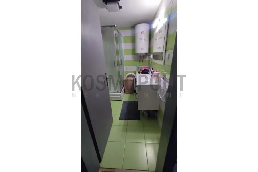 Manje kupatilo sa tuš kabinom i bojlerom na zidu.