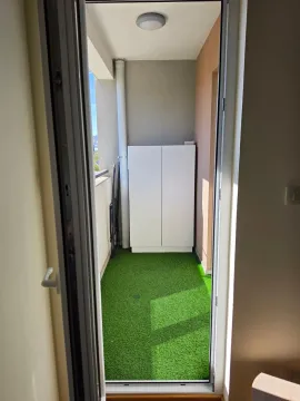 Pogled na uređeni balkon sa vještačkom travom i bijelim ormarićem. - image 11