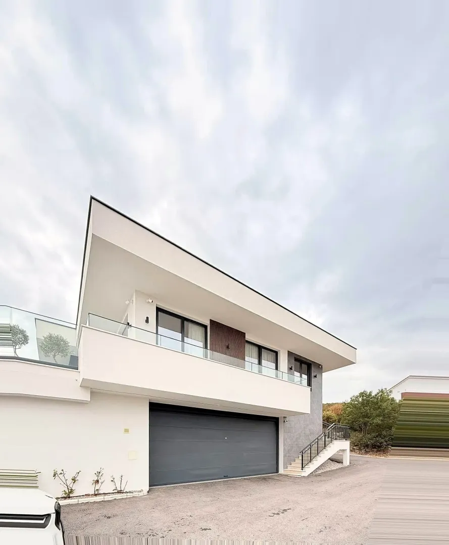 Exterior of a modern two-story house with a ground-floor garage and an upper-floor terrace.
