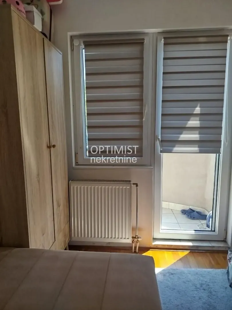 Pogled na deo spavaće sobe sa drvenim ormanom, prozorom i izlazom na terasu.