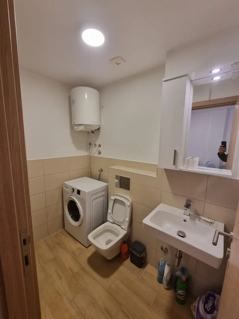 Manje kupatilo sa tuš-kabinom, umivaonikom, WC šoljom i mašinom za veš.