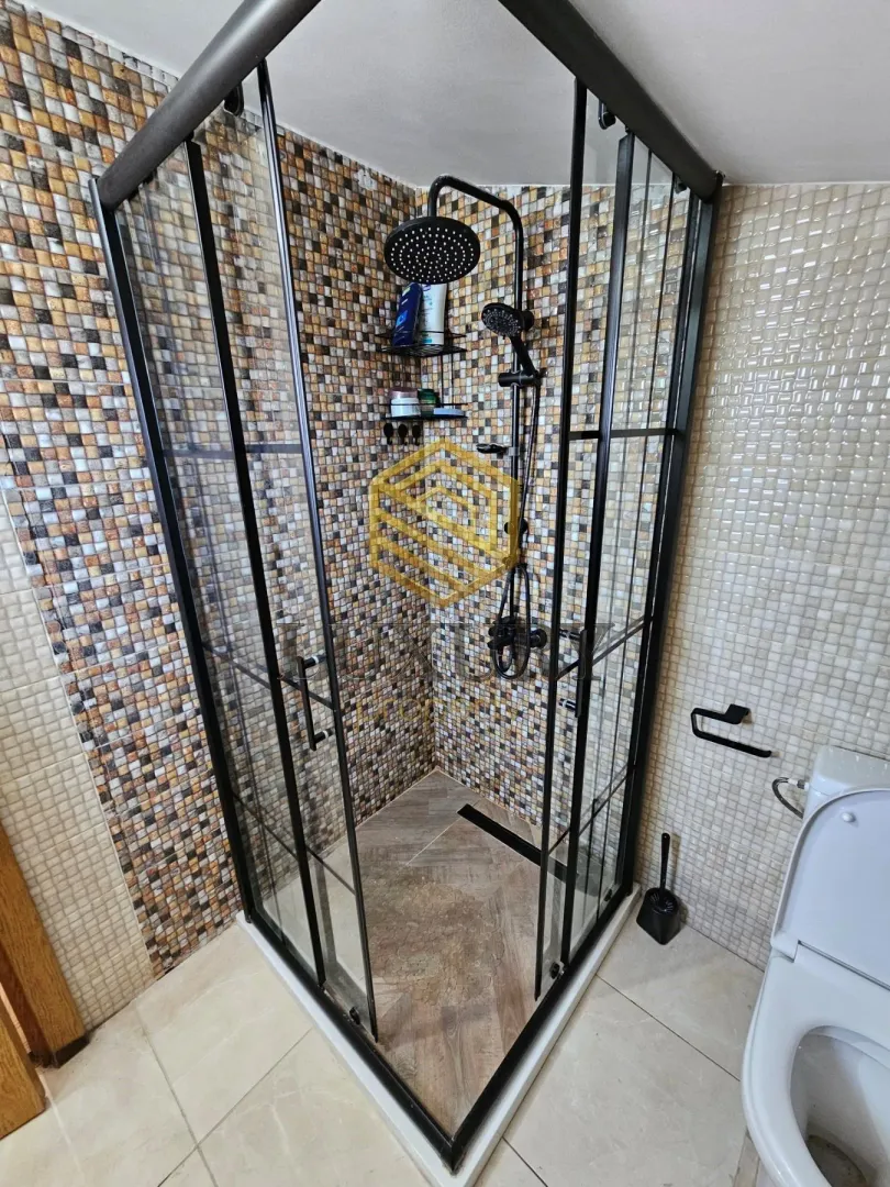 Moderne kupatilo sa tuš kabinom i crnim slavinama.