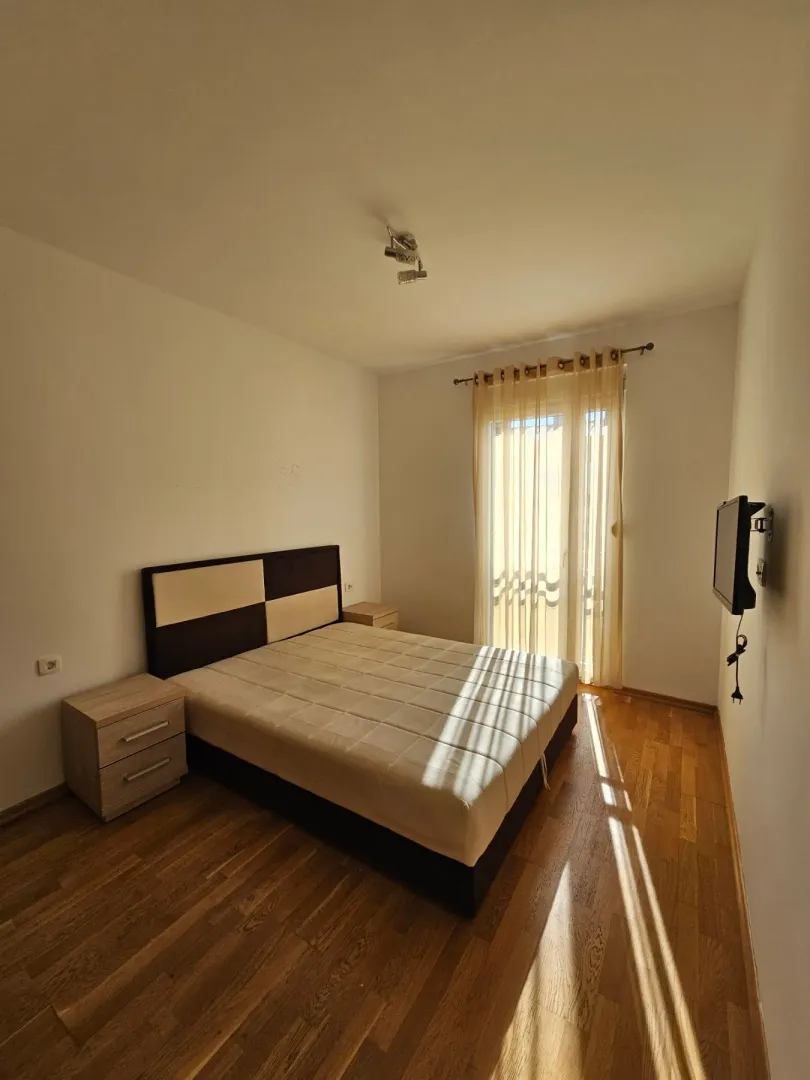 Spavaća soba sa bračnim krevetom, noćnim stočićima i prozorom sa zavjesama.