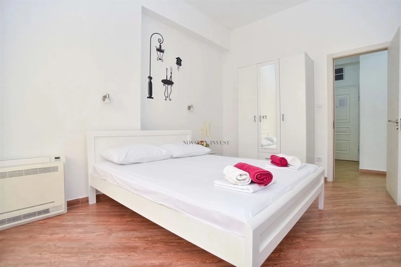 Bright bedroom with a white bed, wardrobe, and wooden flooring.