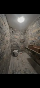 Kupatilo obloženo kamenim pločicama sa umivaonikom i šoljom. - image 6