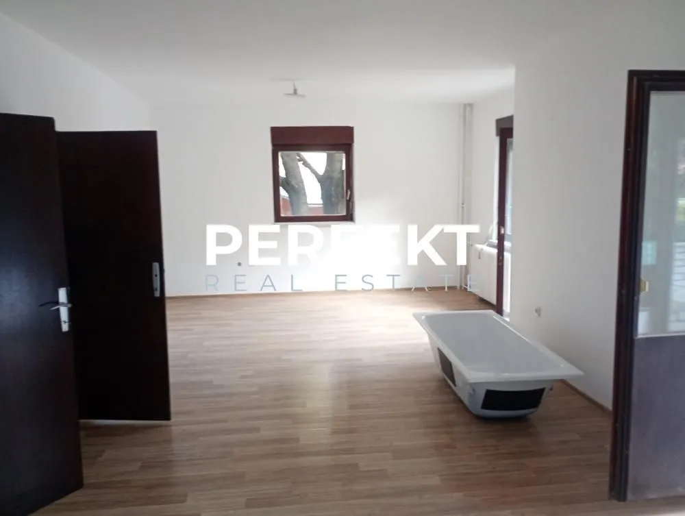 Prazna prostorija sa laminatnim podom i kadom na sredini.