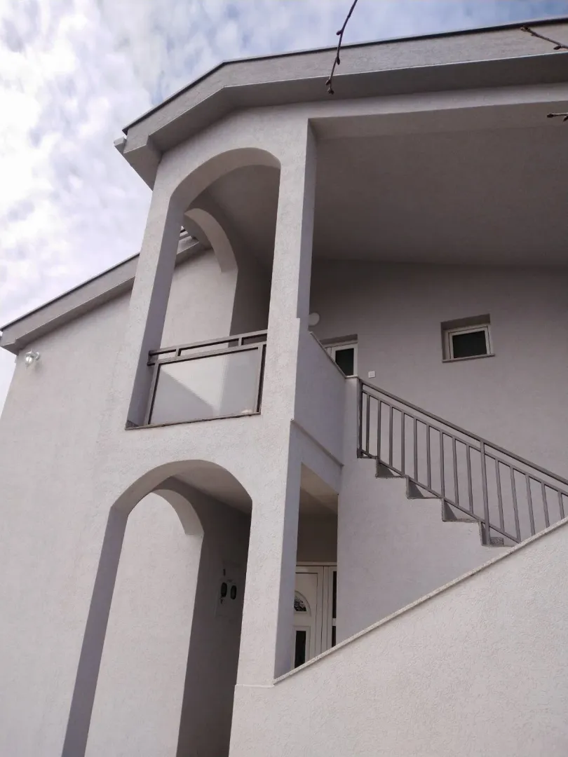 Exterior view of a two-story house featuring arched architectural details and outdoor stairs.
