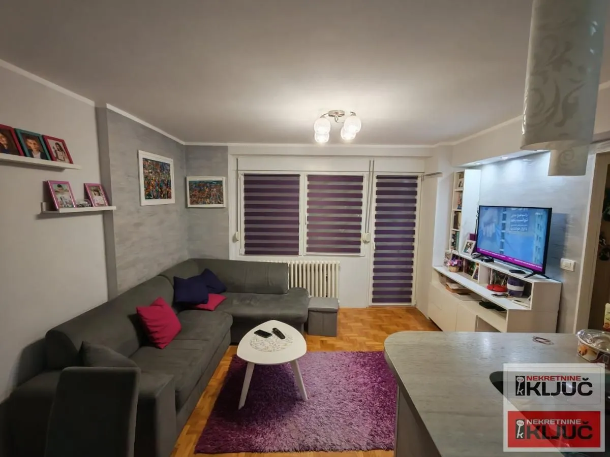 Dnevna soba sa ugaonom garniturom, stočićem i televizorom.
