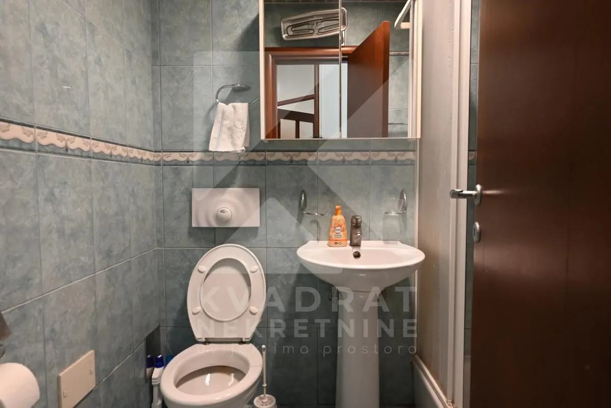 Smaller tiled bathroom with a toilet, washbasin, and mirror cabinet.