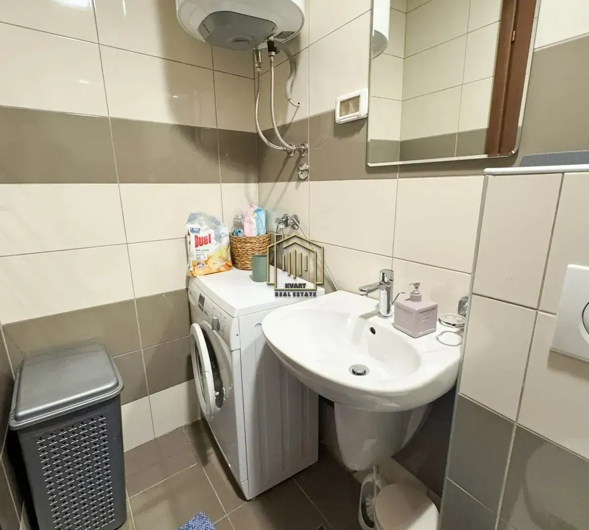 Manje kupatilo sa umivaonikom, veš mašinom i bojlerom na zidu.