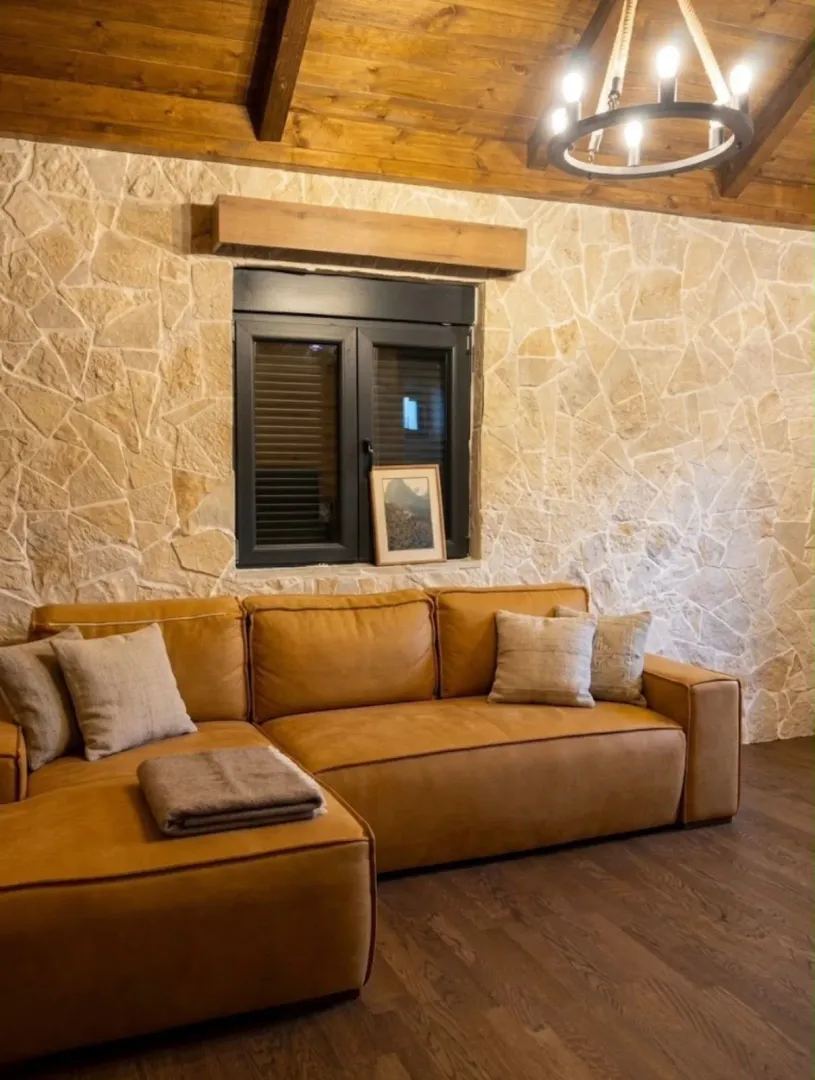 Living room with a leather sofa, stone wall, and wooden ceiling.