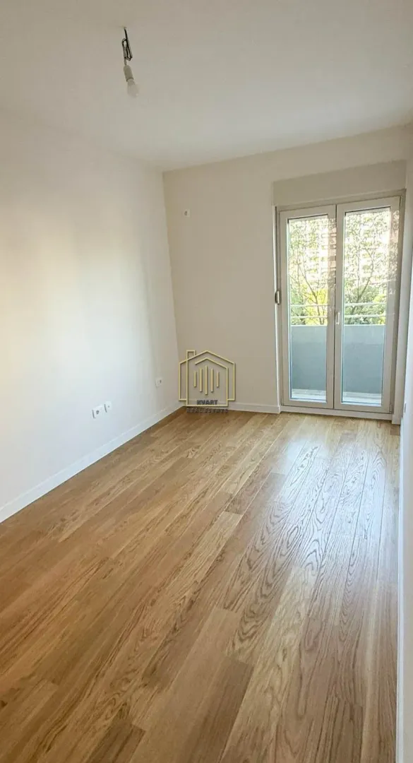 Prazna soba sa drvenim podom i izlazom na terasu.