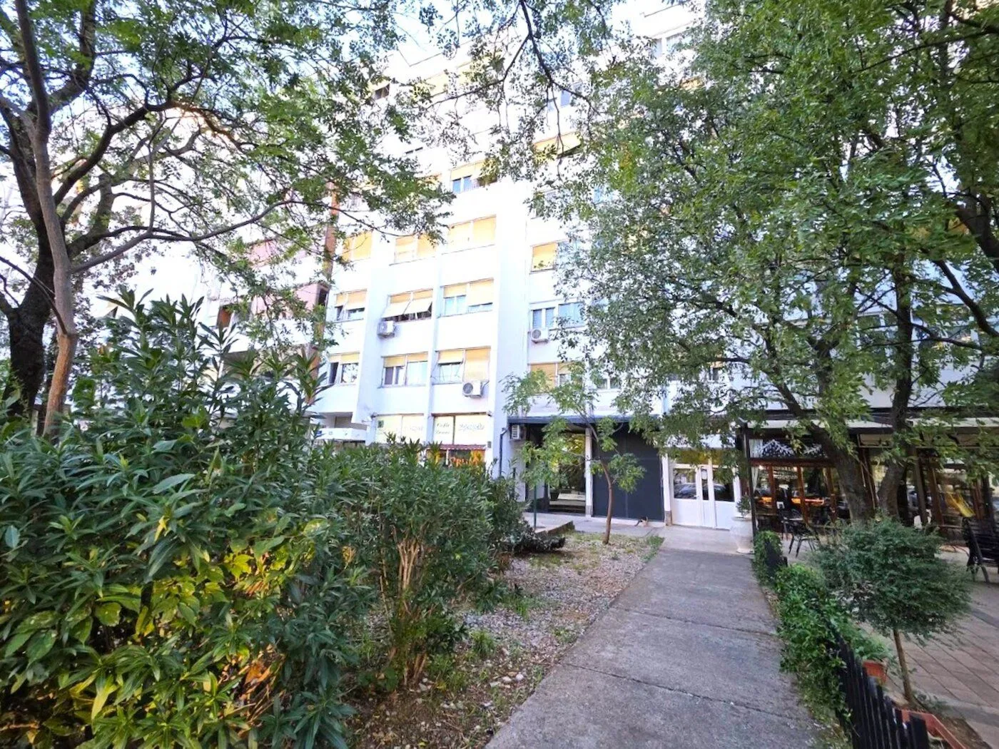 Pogled na fasadu stambene zgrade sa uređenim dvorištem i stazom.