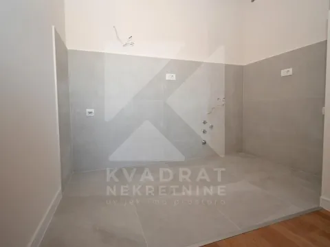 Nenamješten dio kuhinje sa sivim zidnim pločicama i pripremljenim priključcima za vodu i struju. - image 4