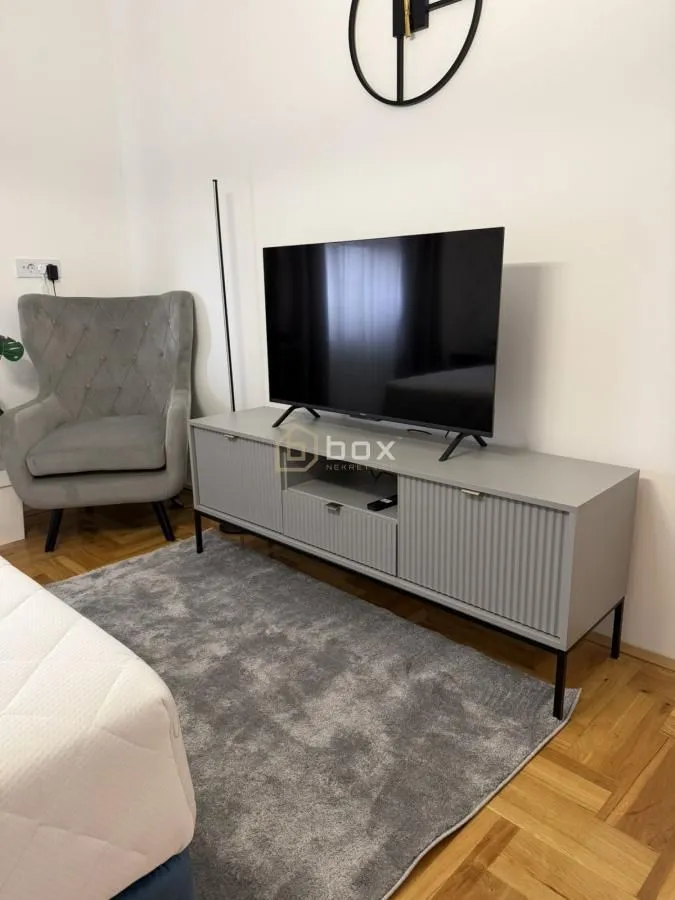 Spavaća soba sa TV-om, komodom i foteljom.