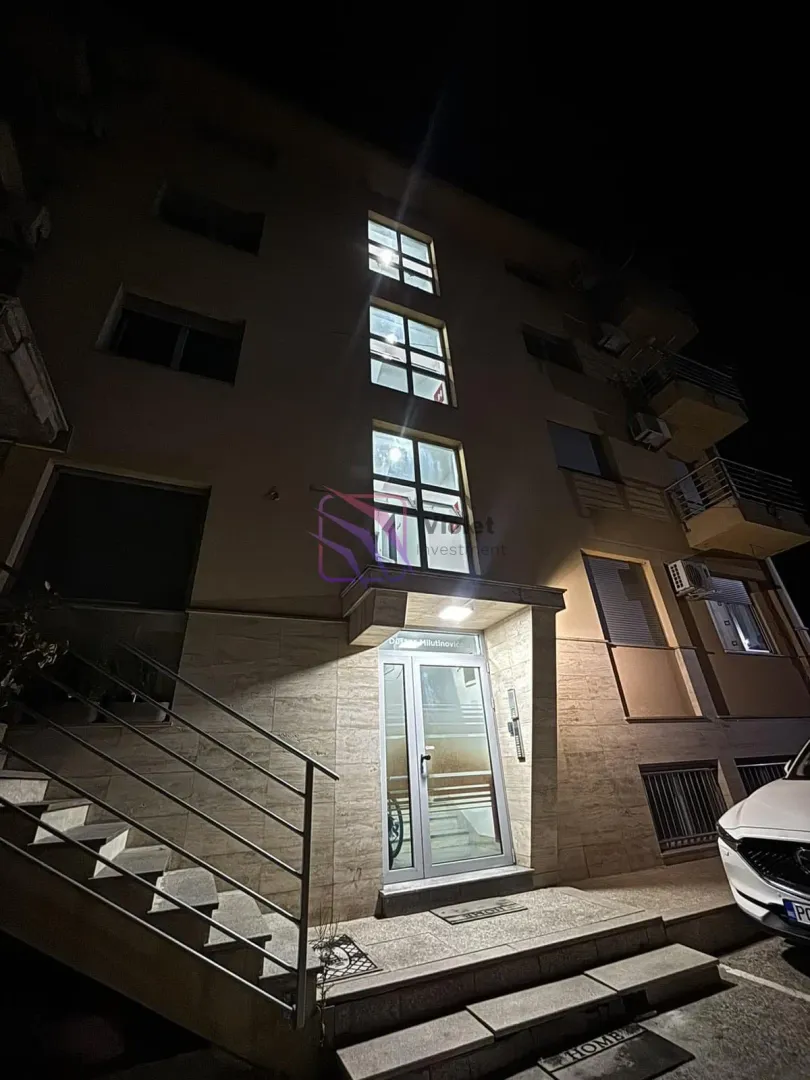 Night view of the illuminated entrance and facade of an apartment building with stairs.