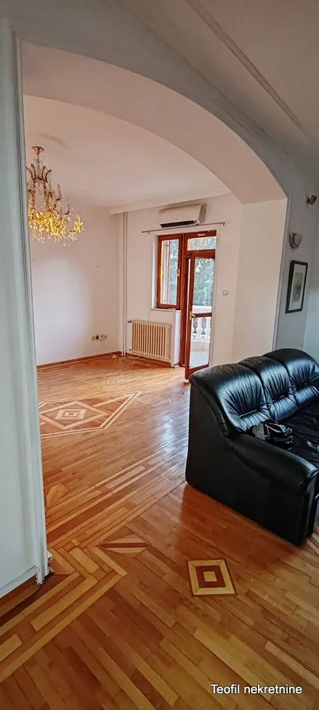 Living room with hardwood flooring and a black leather sofa, with access to the terrace.