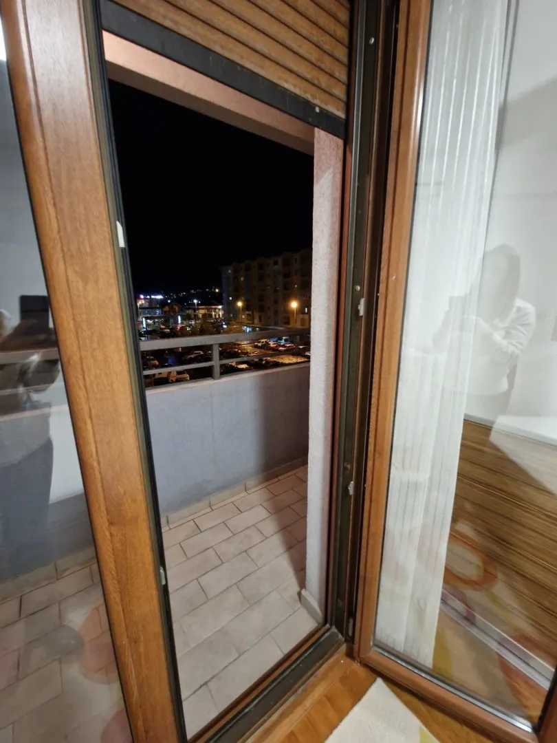 Pogled na balkonski prostor i grad noću kroz otvorena vrata.
