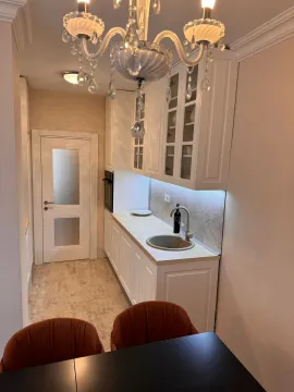 Small white kitchen with a sink, countertops, and a chandelier above. - image 2